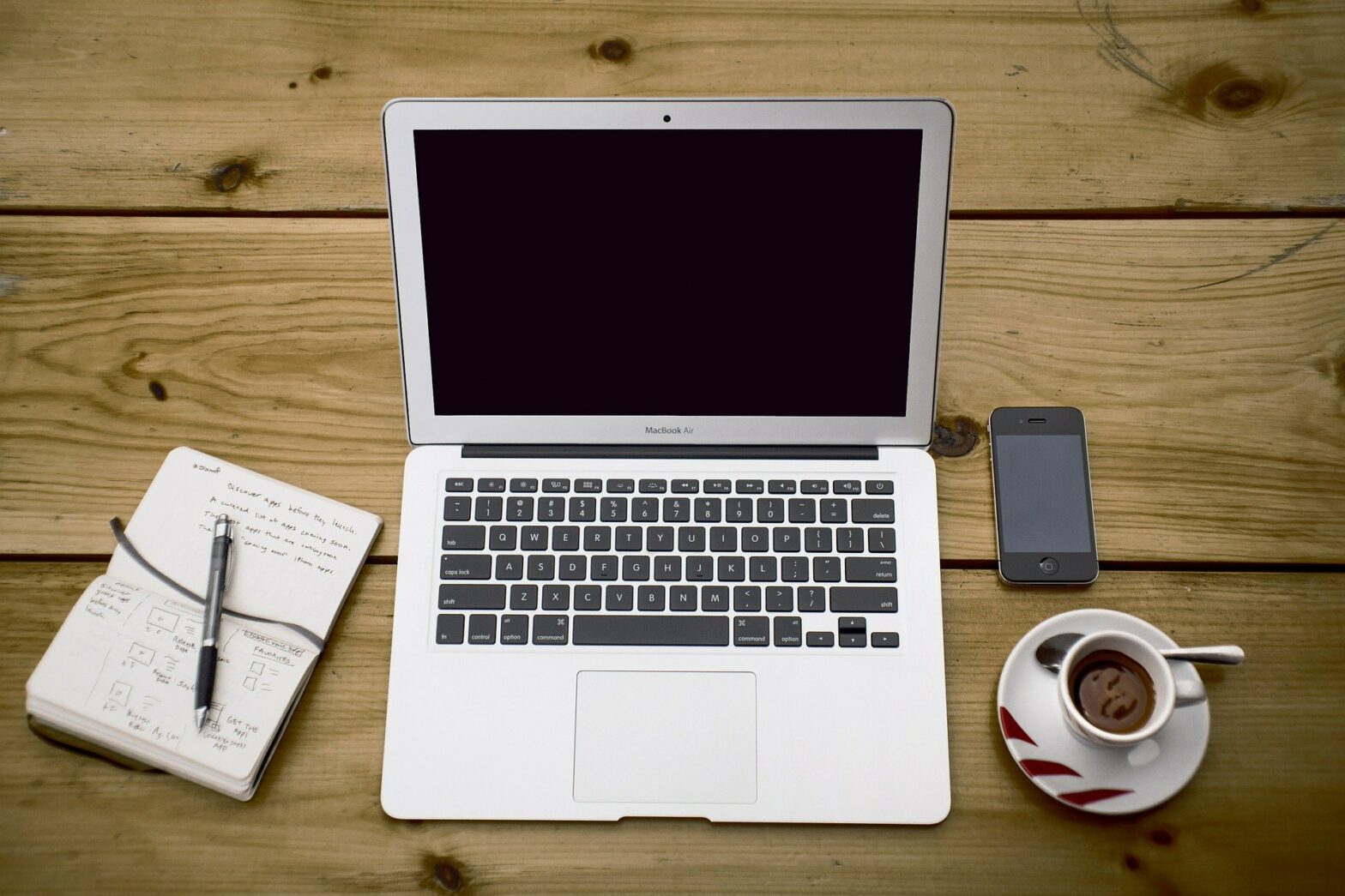 Laptop, Kaffee, Notizbuch und Smartphone auf dem Tisch